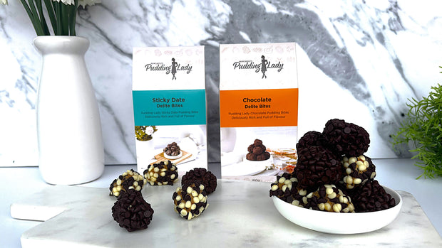 Two boxes of 'Pudding Lady' Delite Bites on a marble surface with decorative elements.