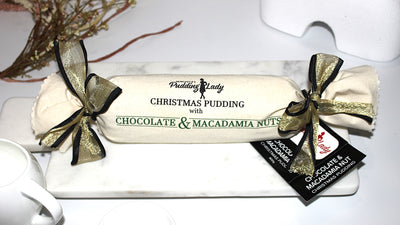 Christmas pudding with chocolate and macadamia nuts, wrapped in black and gold ribbon, on a white plate.