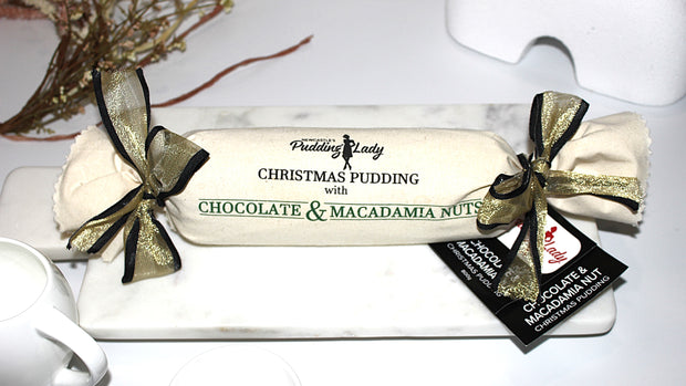 Christmas pudding with chocolate and macadamia nuts, wrapped in black and gold ribbon, on a white plate.