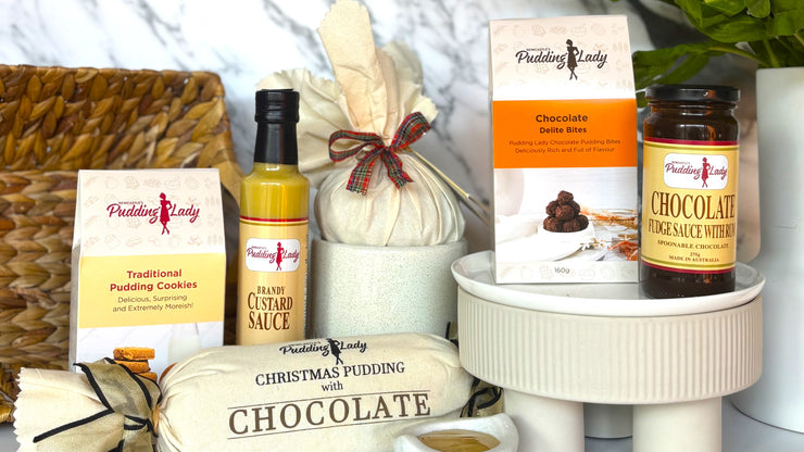 Collection of pudding lady products including cookies, sauce, and pudding on a white surface.