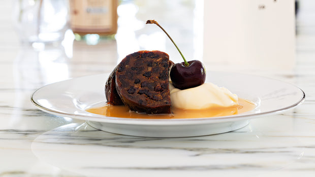 Choc Rum & Raisin log pudding plated with brandy custard, cream and a cherry