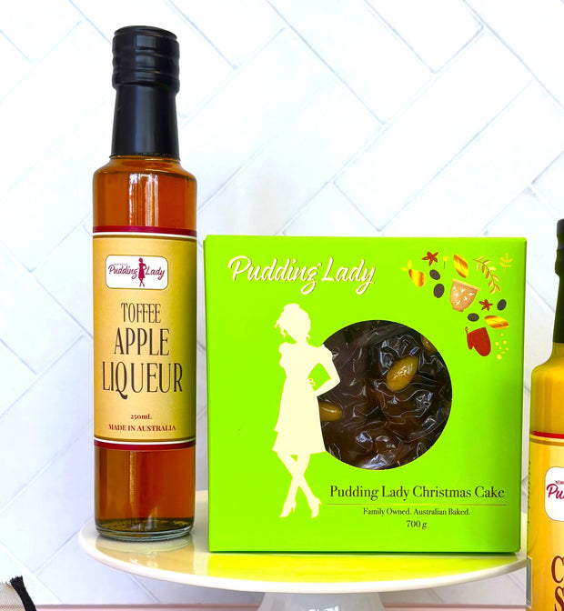 Bottle of toffee apple liqueur next to a Pudding Lady Christmas Cake boxed