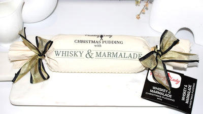 Christmas pudding with whisky and marmalade, wrapped in white calico with gold ribbon, on a white background.