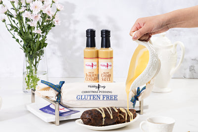 Hand pouring custard over a gluten free pudding log sliced on a plate 