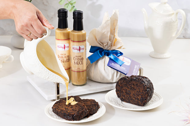 Two bottles of rum custard and brandy custard sauce with two pieces of pudding on a white surface.