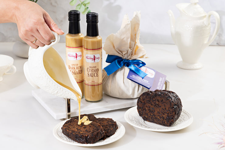 Two bottles of rum custard and brandy custard sauce with two pieces of pudding on a white surface.