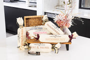 Assorted Christmas pudding logs wrapped in calico with a woven basket on a kitchen counter.