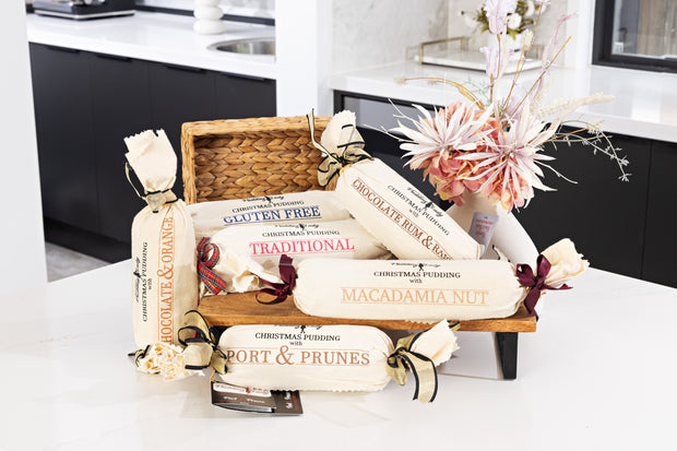 Assorted Christmas pudding logs wrapped in calico with a woven basket on a kitchen counter.