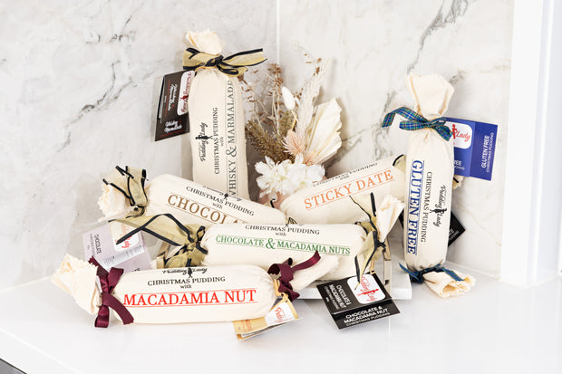 Assorted log puddings including macadamia nut with calico packaging on a marble surface