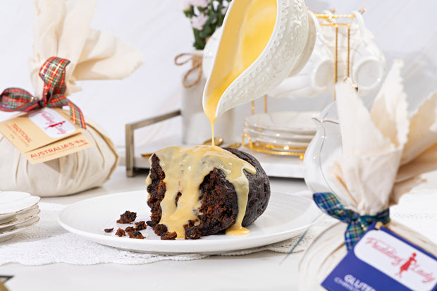 Gluten free pudding with custard being poured over it on a table setting.